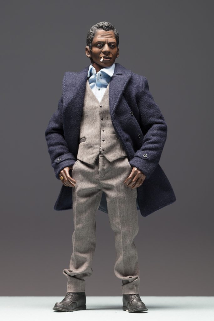 8 inch figurine of James Baldwin wearing a blue coat, hands in pockets and smoking a cigarette.